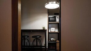 A kitchenette with a microwave, a small fridge, and a wooden bar counter with two stools. - Guesthouse Kinoya (Kyoto)