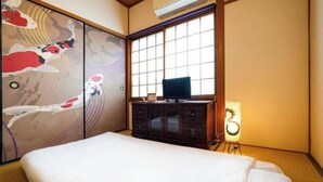A traditional Japanese-style room with tatami flooring, a bed, a television on a cabinet, and a shoji screen with koi fish artwork. - Guesthouse Kinoya (Kyoto)