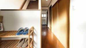 A hallway with wooden flooring, a shoe rack with slippers, and a wooden door. - Guesthouse Kinoya (Kyoto)