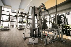 Een sportschool met diverse fitnessapparaten, loopbanden en een rekbank.