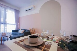A dining area with a table set for two, a sofa, and a window with curtains.