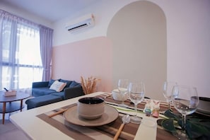 A dining area with a table set for two, a sofa, and a window with curtains.