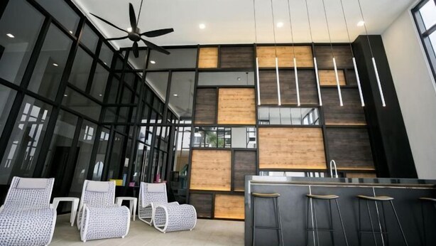 A modern kitchen with a bar area, large windows, and ceiling fans. - Econest Apartment By The One - Educity Ecobotanic (Gelang Patah)