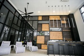 A modern kitchen with a bar area, large windows, and ceiling fans. - Econest Apartment By The One - Educity Ecobotanic (Gelang Patah)