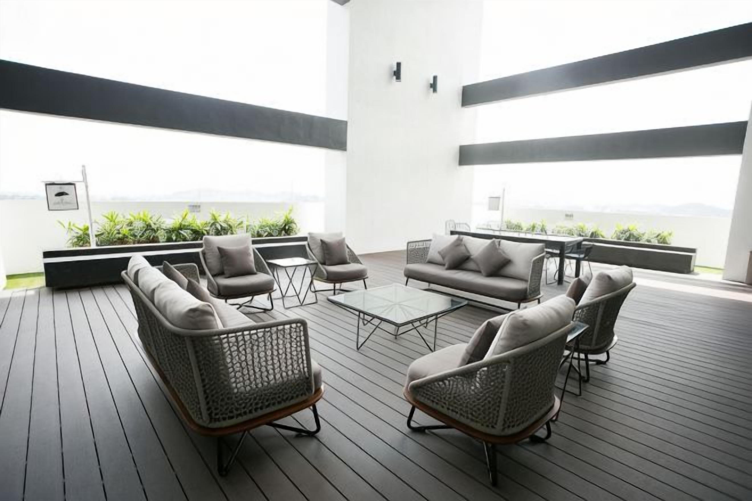 A rooftop lounge with wicker furniture, a glass coffee table, and a view of the sea.