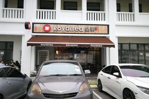A building with a sign for 'Royaltea' and two parked cars. - Econest Apartment By The One - Educity Ecobotanic (Gelang Patah)
