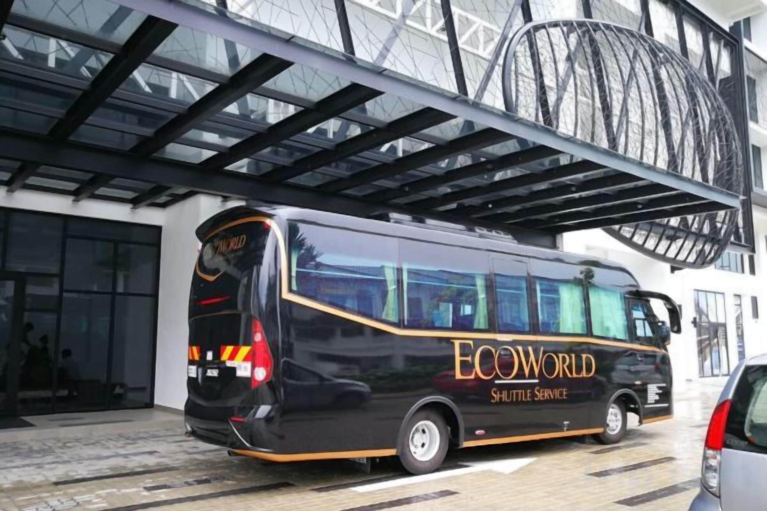 A black shuttle bus with 'ECOWORLD SHUTTLE SERVICE' written on the side parked in front of a building with a large glass facade.