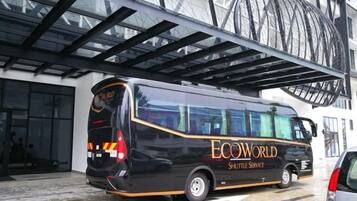 A black shuttle bus with 'ECOWORLD SHUTTLE SERVICE' written on the side parked in front of a building with a large glass facade.