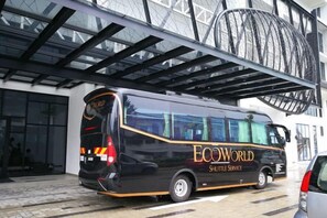A black shuttle bus with 'ECOWORLD SHUTTLE SERVICE' written on the side parked in front of a building with a large glass facade.