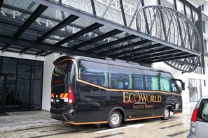 A black bus with 'ECOWORLD' and 'Sustainable Service' written on it, parked in front of a building with a glass facade and a metal structure above.