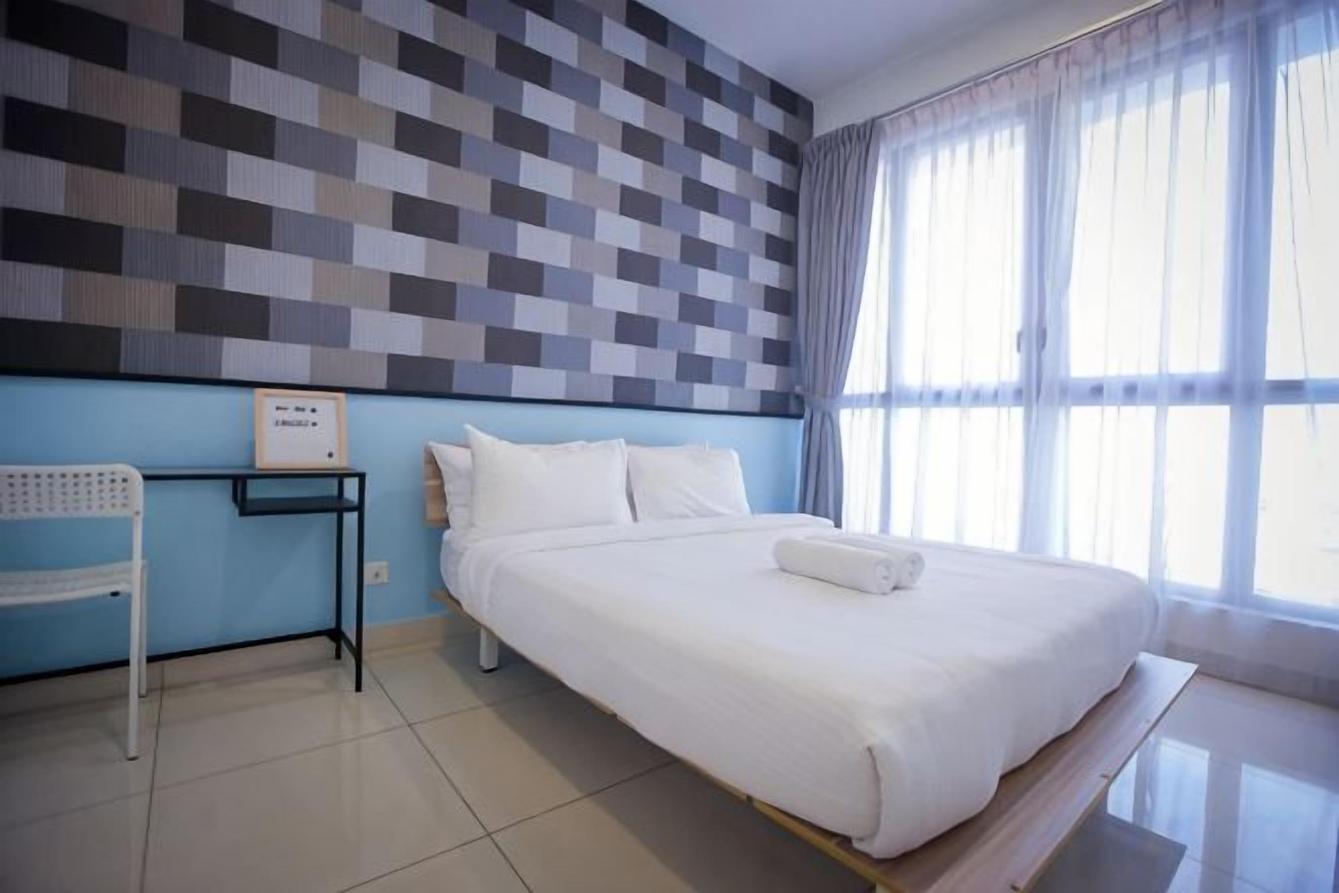 A hotel room with a large bed, a bedside table, a chair, and a view of the outdoors through a window.