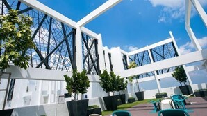 A modern building with large windows, outdoor seating, and greenery. - Econest Apartment By The One - Educity Ecobotanic (Gelang Patah)