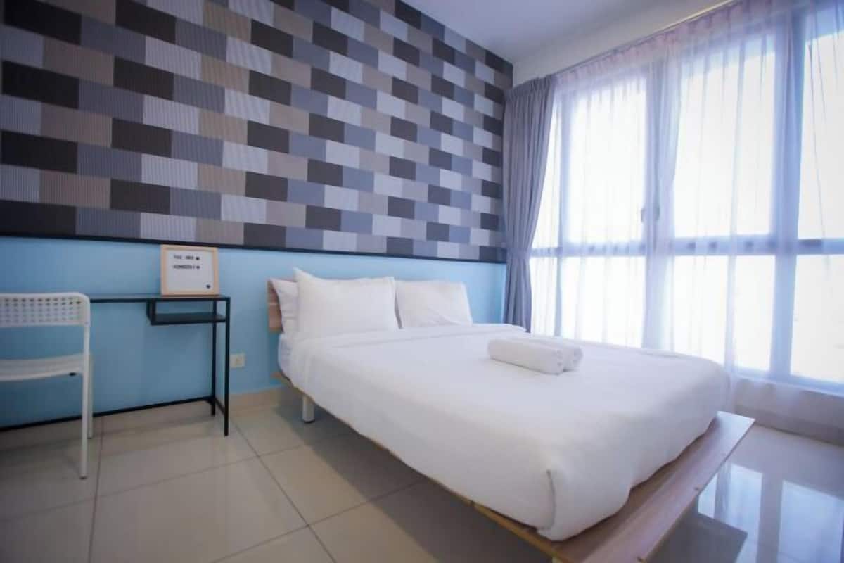 Ein Hotelzimmer mit einem großen Bett, einem kleinen Tisch, einem Sessel und einem Fenster mit Vorhängen.