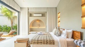 A modern bedroom with a large bed, a bedside table, and a view of the outdoors. - Villa Serai 5br to the beach (Bali)