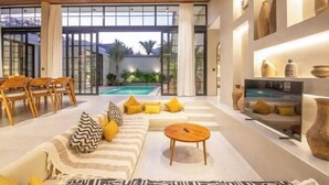 A modern living room with a sofa, chairs, a coffee table, and a pool view. - Villa Serai 5br to the beach (Bali)