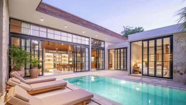 A modern house with a swimming pool, large windows, and a well-lit interior. - Villa Serai 5br to the beach (Bali)