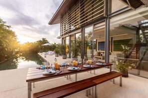 Zona d'exterior per dinar amb taula de fusta preparada per a dos, amb vista a una piscina i un edifici modern amb grans finestrals.