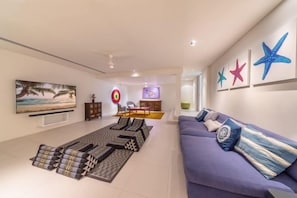 A modern living room with a sofa, a coffee table, and a flat-screen TV. There is a painting on the wall and a starfish decoration. - Sava Villa 7 Villa Aqua (Takua Thung)