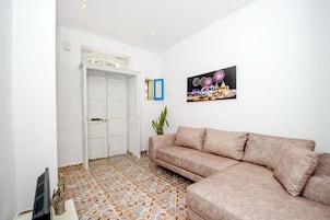 A living room with a beige sofa, a tiled floor, a white door, and a framed picture on the wall.