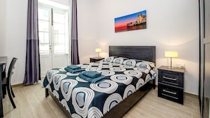 Una habitación de hotel con cama, dos mesitas de noche, un escritorio y una silla.