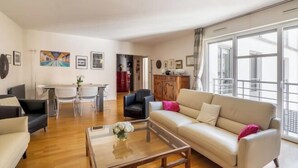 A spacious living room with a sofa, coffee table, and dining area. - Village Vision (Paris)