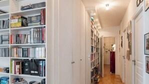 A hallway with bookshelves on both sides, a wooden floor, and a door at the end. - Village Vision (Paris)