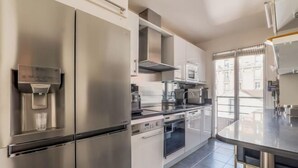 A modern kitchen with stainless steel appliances, a built-in oven, and a large window providing a view of the city. - Village Vision (Paris)