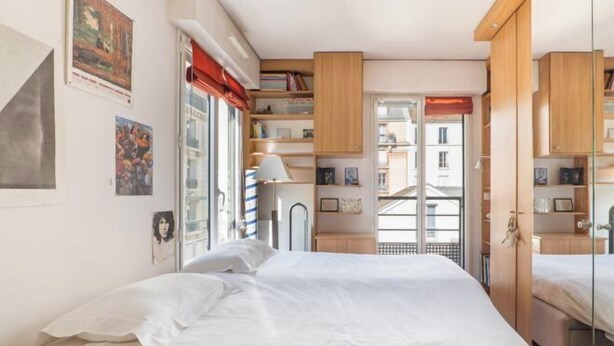 A bedroom with a bed, a window with curtains, a bookshelf, and a door leading to another room. - Village Vision (Paris)