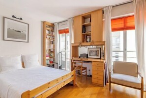 A bedroom with a bed, a desk, a chair, a bookshelf, and a window with curtains. - Village Vision (Paris)
