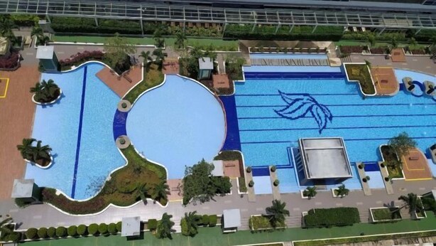 Vista aérea de un complejo de piscinas con varias albercas, rodeado de áreas ajardinadas y senderos.