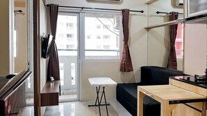 Un espacio habitable compacto con kitchenette, una pequeña mesa de comedor, un sofá y un televisor montado en la pared.