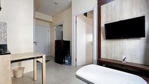 Habitación de hotel con una televisión de pantalla plana montada en la pared, un escritorio de madera, una plancha pequeña y piso de baldosas.