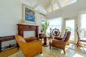 A room with a fireplace, two leather armchairs, a table with a ship's wheel, and a large window overlooking the sea.
