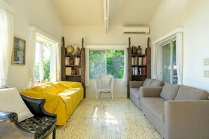 Une pièce avec un canapé jaune, un canapé gris, un fauteuil blanc et une bibliothèque.