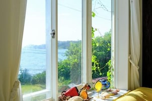 A room with a large window overlooking a body of water and greenery.