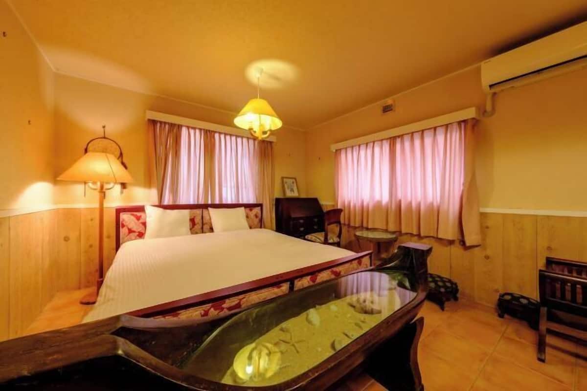 Une chambre d’hôtel avec un lit, un bureau, une chaise, une lampe et une fenêtre avec des rideaux.