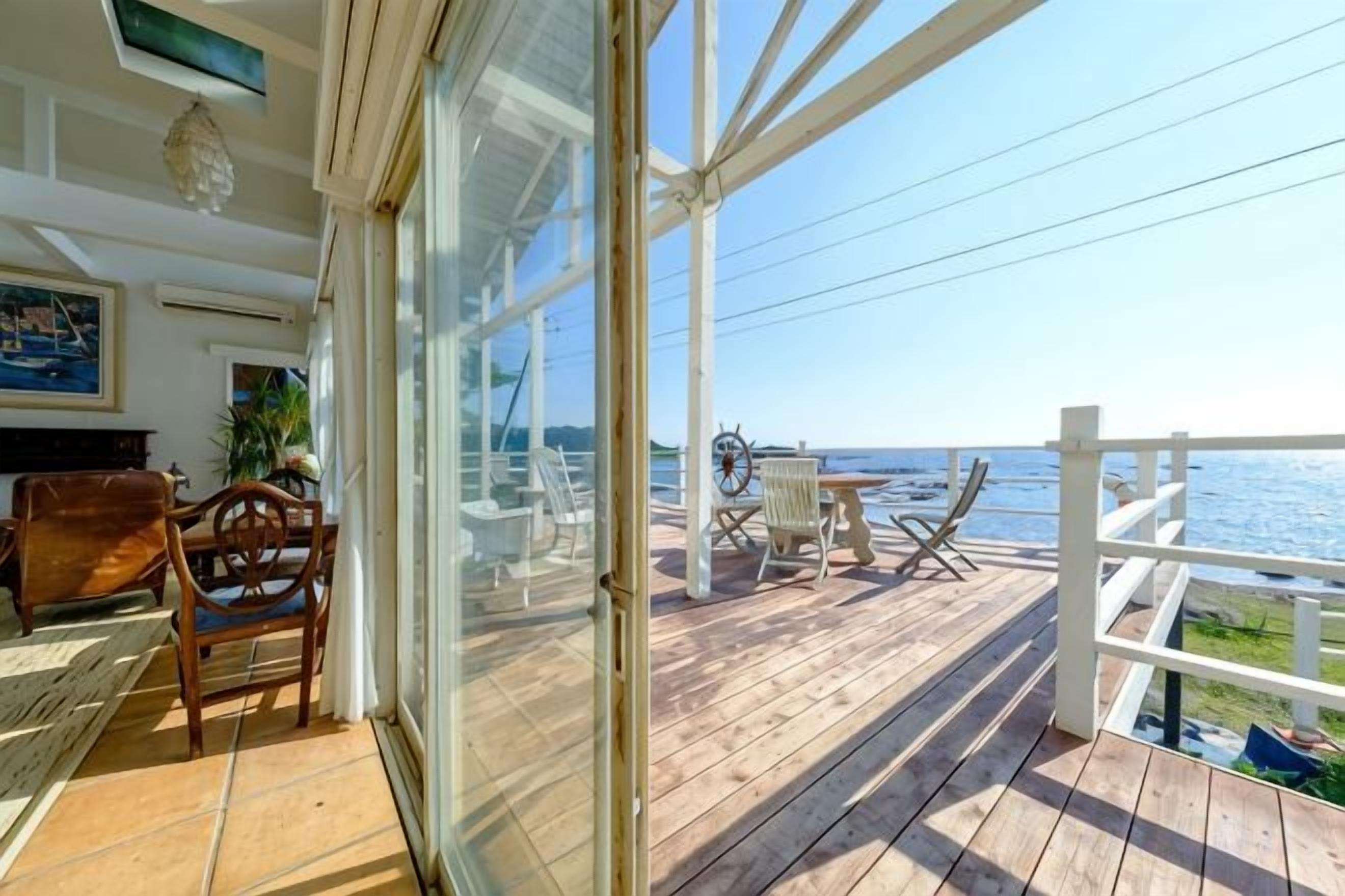 A wooden deck with outdoor furniture, a glass door leading to a room, and a view of the sea.