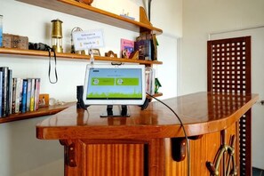 Un comptoir en bois, sur lequel est posé un écran d’ordinateur affichant une interface verte, est entouré de livres et d’un panneau indiquant une zone d’attente.