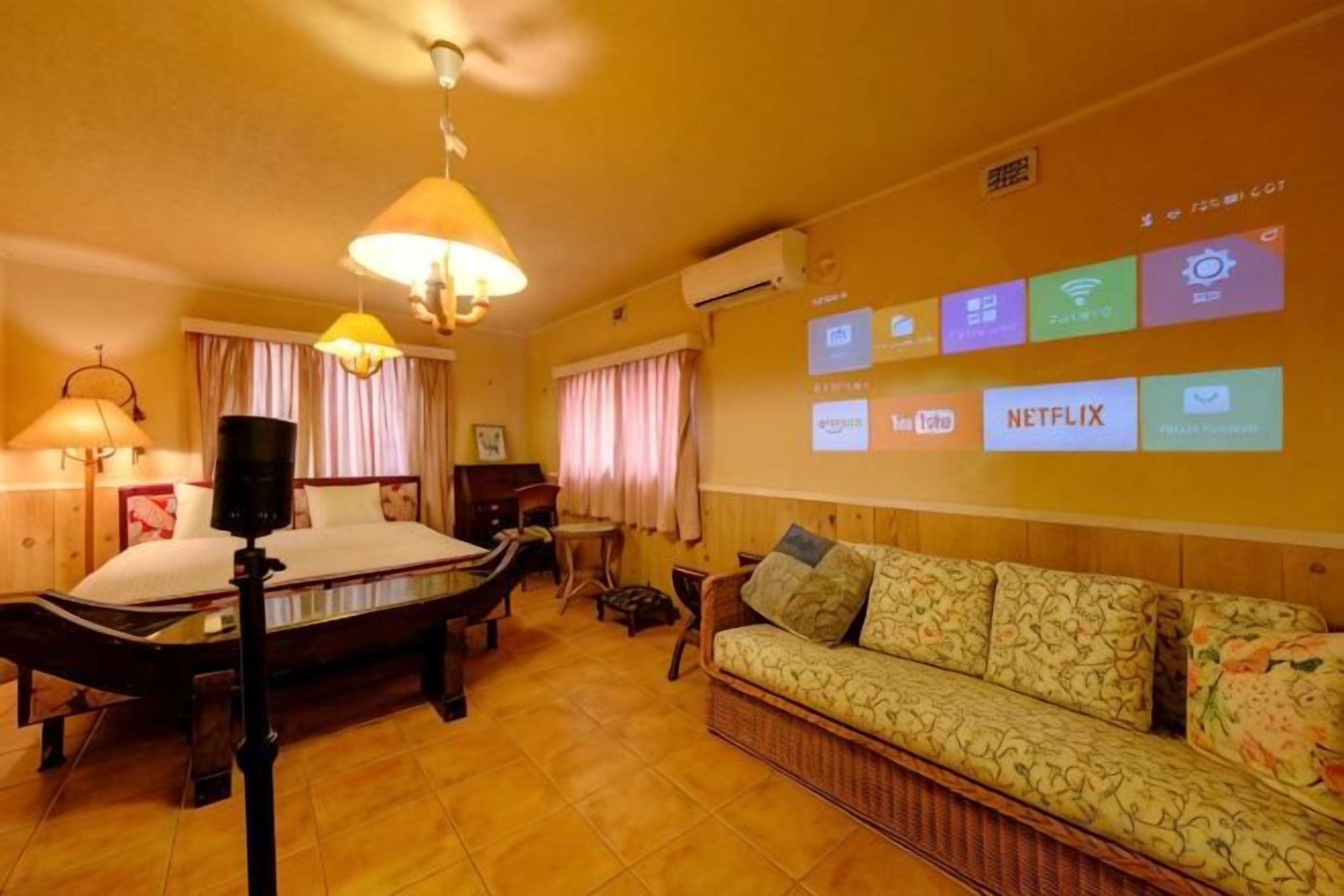A hotel room with a bed, a sofa, a desk, and a wall-mounted TV displaying various channels.