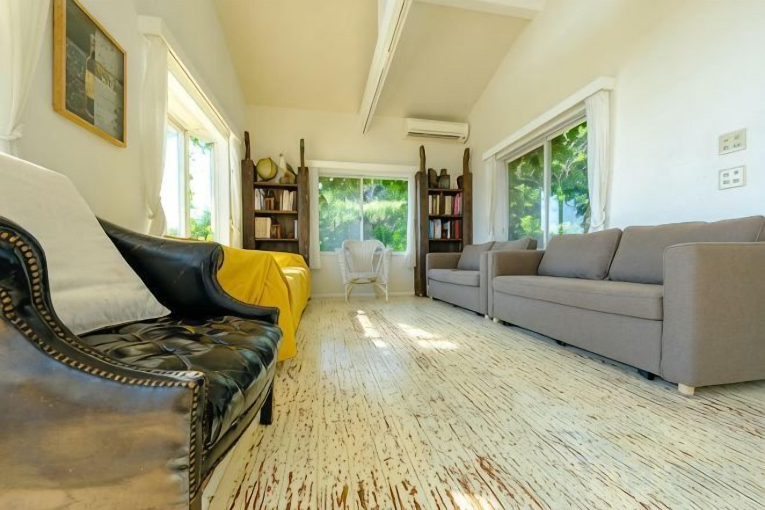 A living room with a black leather sofa, a grey sofa, and a yellow-covered chair. There are bookshelves and a white table in the background.