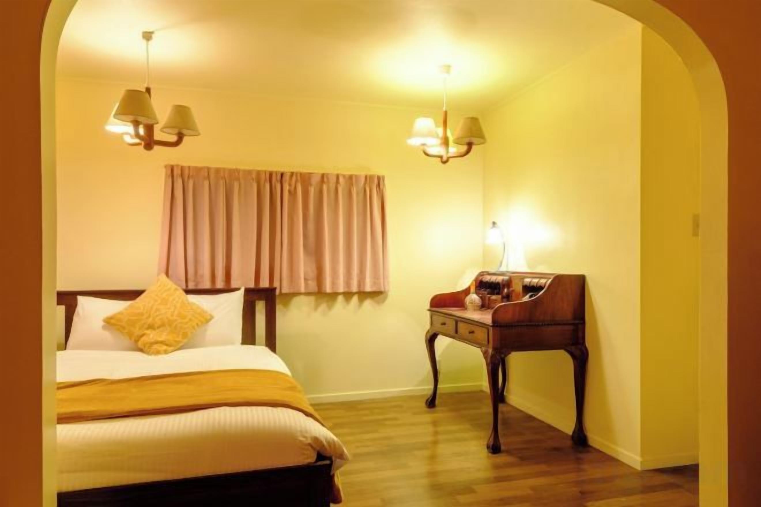 A hotel room with a bed, a desk, and two wall-mounted lamps.