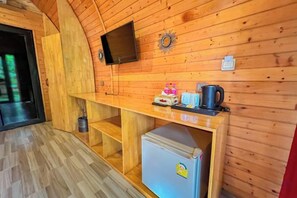 A wooden interior with a flat-screen TV, a wooden bench, a refrigerator, and a small table with cups and a kettle. - Moly Resort (Kampot)