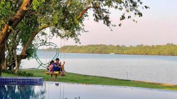 A couple sitting on a swing by a pool with a lake view.