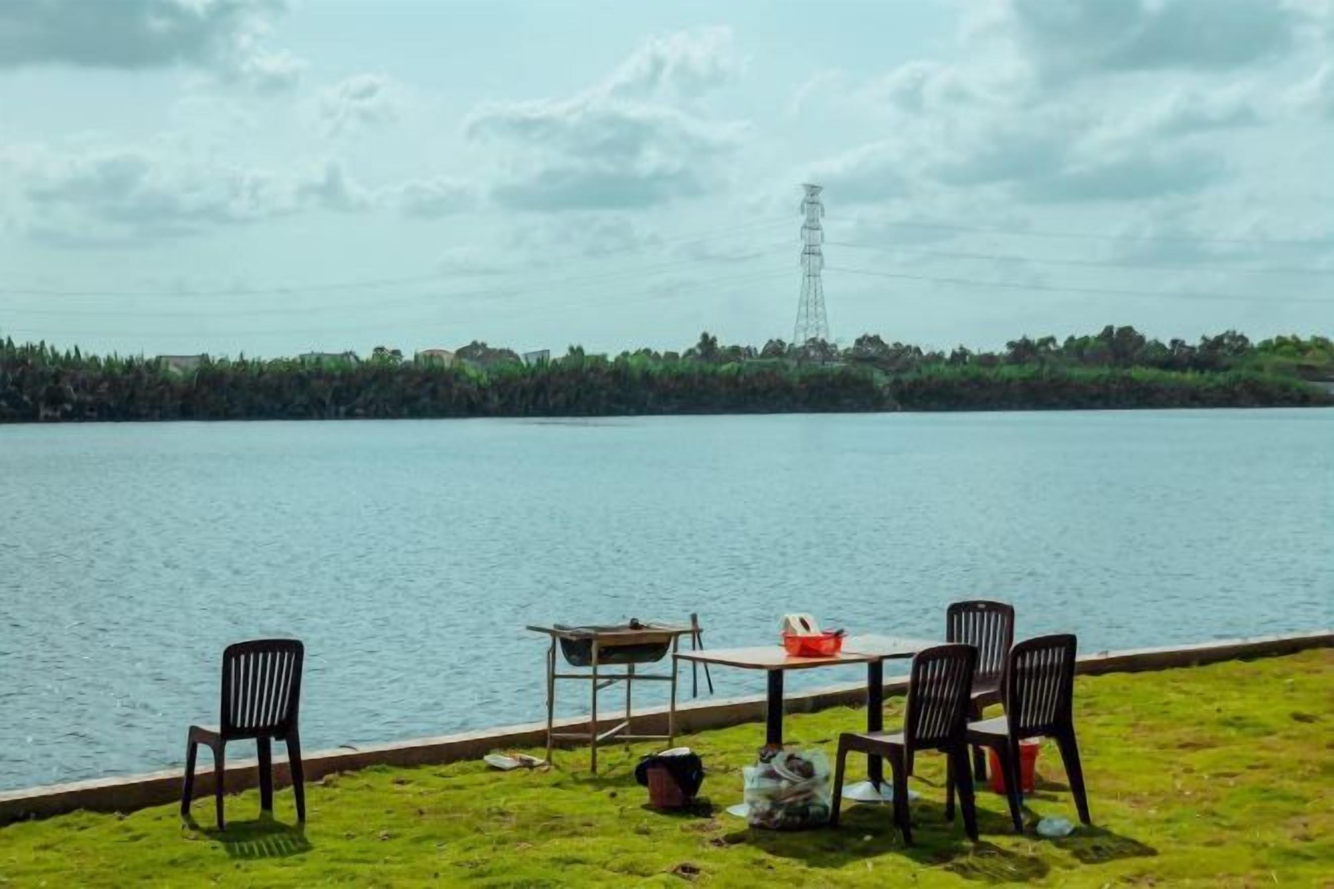 A lakeside view with a table and chairs, a grassy area, and a distant power line tower.