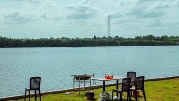 A lakeside view with a table and chairs, a grassy area, and a distant power line tower.