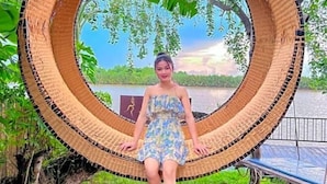A person sitting in a circular wicker chair outdoors with a natural landscape in the background. - Moly Resort (Kampot)