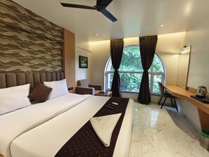 A hotel room with a large bed, a desk, a chair, and a view of greenery through the window. - The Golden Arc (Pune)