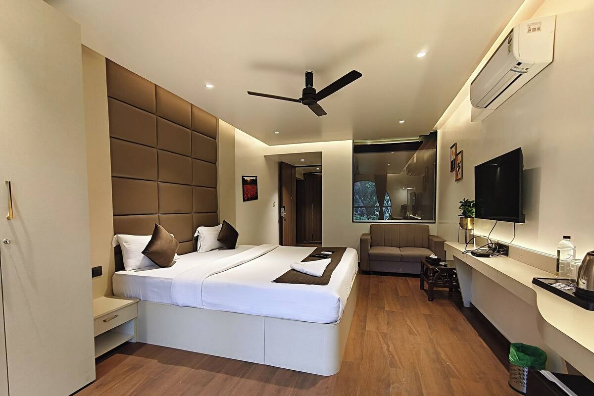 A modern hotel room with a large bed, a sofa, a desk, and a TV.