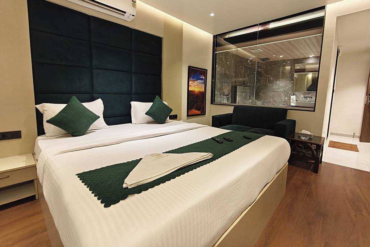 A modern hotel room with a large bed, a dark headboard, a large mirror, and a view of the bathroom.