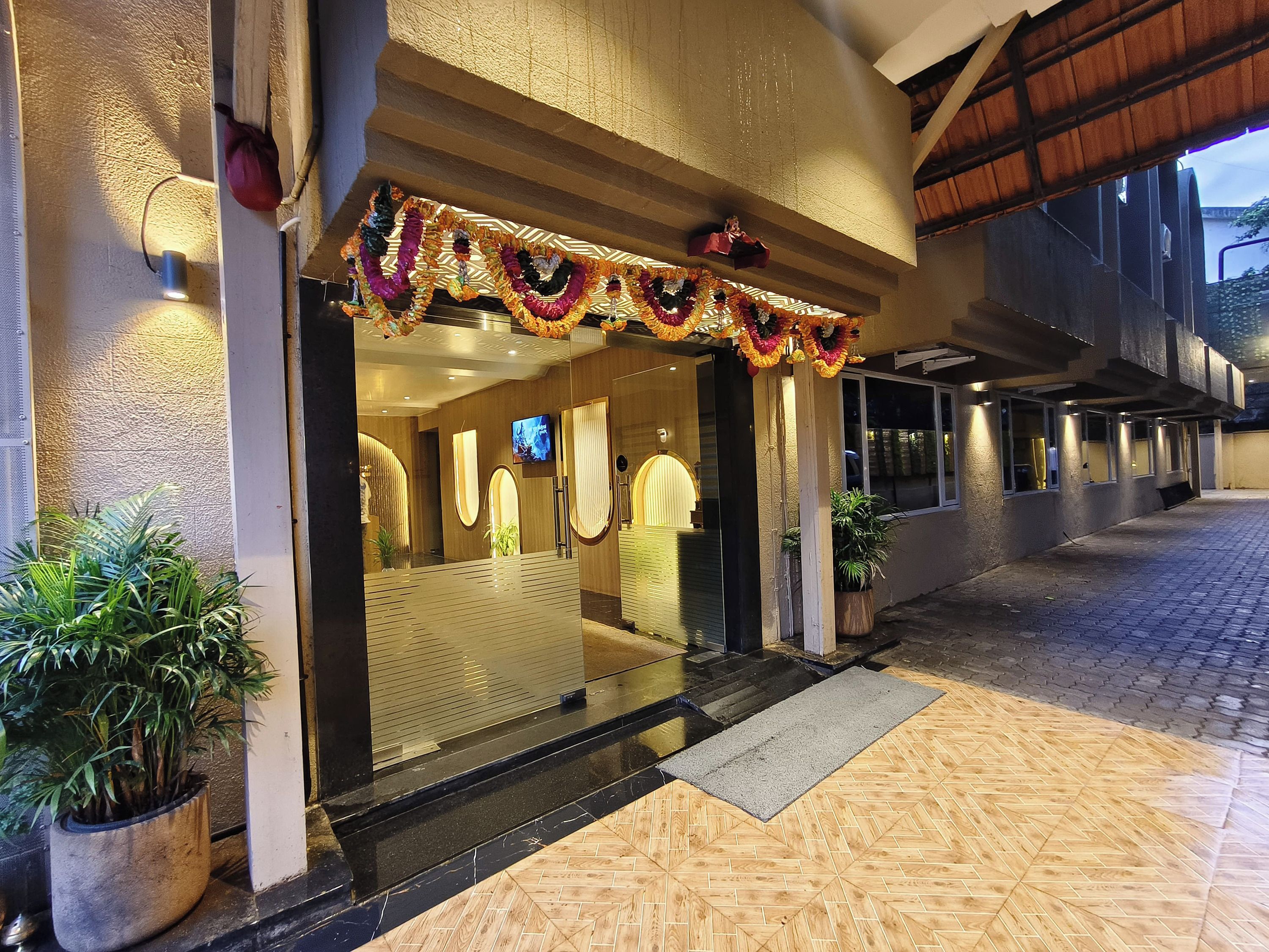 A hotel entrance with a glass door, potted plants, and a tiled walkway.